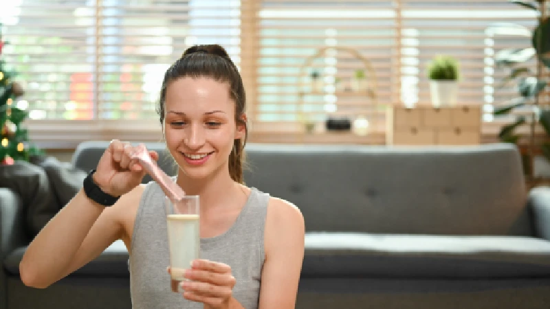 Žena meša kolagen u prahu u čaši vode kod kuće, priprema suplement za zdravlje kože i zglobova