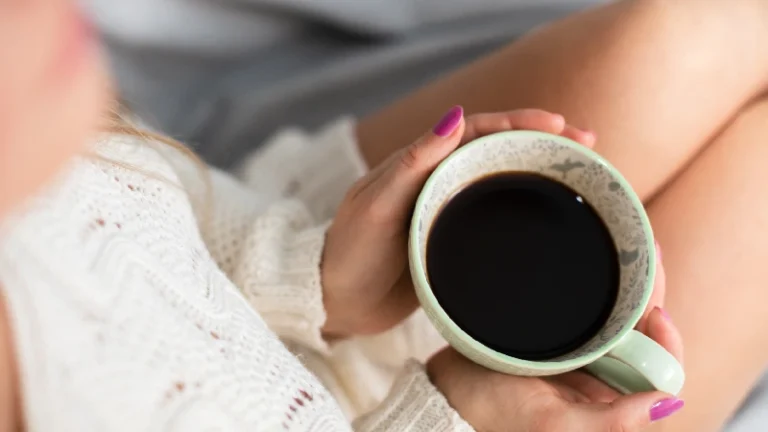 Osoba drži šolju crne kafe u opuštenoj atmosferi, simbol jutarnje rutine, energije i uživanja u toplom napitku, i da kafa utiče na menstruaciju i hormone