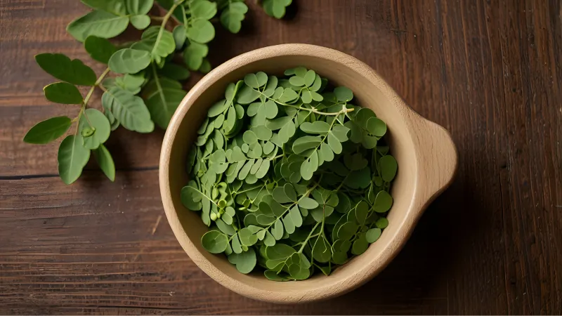 Sveži listovi moringe u drvenoj posudi na drvenoj podlozi, ilustracija biljke moringa i dodatka ishrani proizvod Moringa Ekstrakt za prirodnu podršku energiji i vitalnosti.