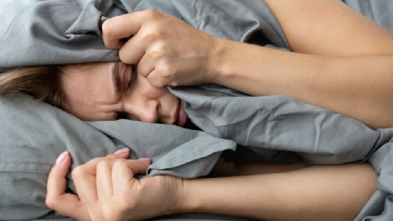 Žena pokriva lice ćebetom u krevetu, budna usred noći – buđenje povezano sa kortizolom i šećerom u krvi